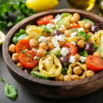 Colorful Chickpea Tortellini Salad served in a bowl, featuring cheese tortellini, chickpeas, cherry tomatoes, cucumber, red onion, and a zesty dressing garnished with fresh parsley.