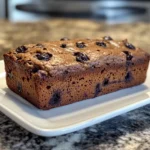 Healthy Blueberry Banana Bread slice topped with fresh blueberries, served on a rustic wooden board.