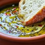 Homemade olive oil bread dip with garlic, balsamic, and fresh herbs served with crusty baguette slices